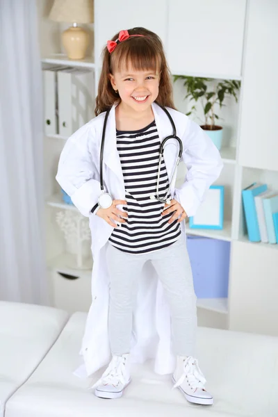 Niña en traje de médico con estetoscopio en el fondo interior de la oficina —  Fotos de Stock