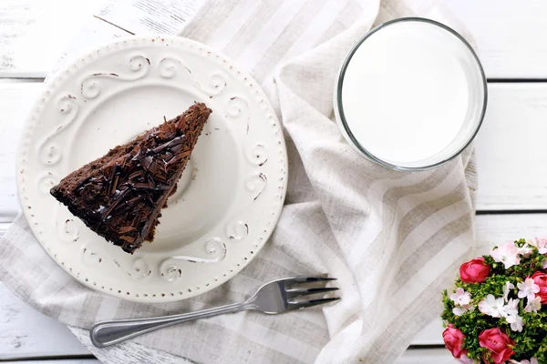 Bolo de chocolate saboroso fatiado em placa e vidro de leite na cor de fundo de mesa de madeira, close-up — Fotografia de Stock