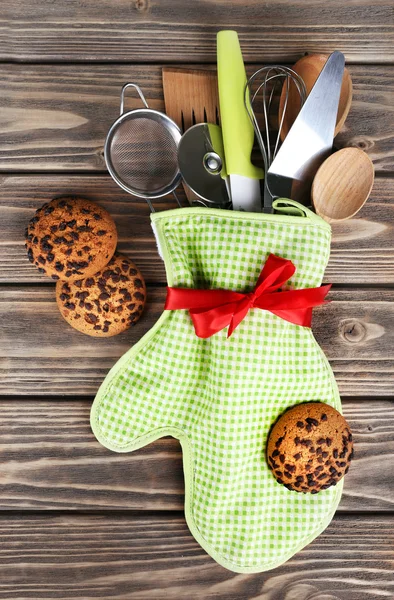 Комплект кухонной утвари в варежке с шоколадным печеньем на фоне деревянных досок — стоковое фото