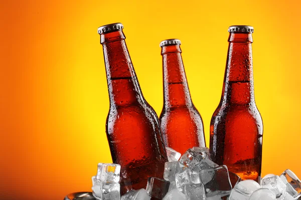 Стеклянные бутылки пива в кубиках льда на цветном фоне — стоковое фото