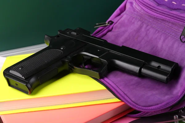 Pistola en la mochila de la escuela de cerca, en el fondo de pizarra —  Fotos de Stock