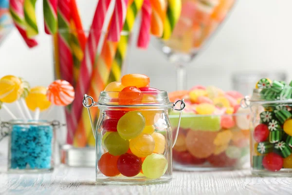 Bunte Bonbons in Gläsern auf Tisch auf hölzernem Hintergrund — Stockfoto