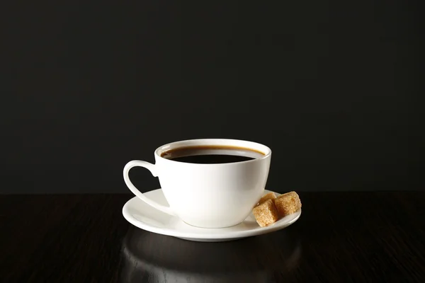 Cup of coffee with lump sugar on wooden table, on dark background — Stock Photo, Image