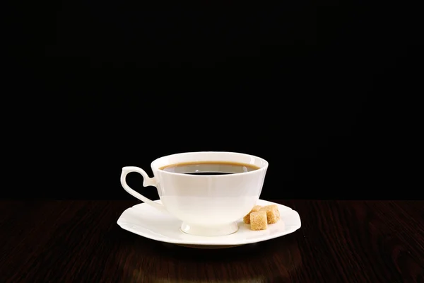 Cup of coffee with lump sugar on wooden table, on dark background — Stock Photo, Image