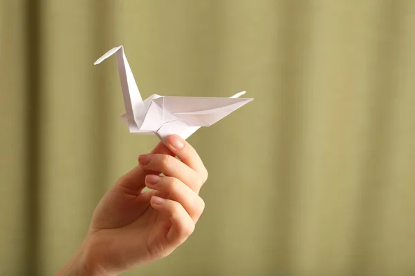 Vrouwelijke hand met papier kraan op onscherpe achtergrond — Stockfoto