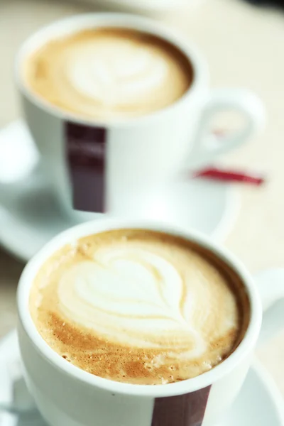 Tazas de capuchino con corazón sobre espuma sobre mesa en cafetería — Foto de Stock