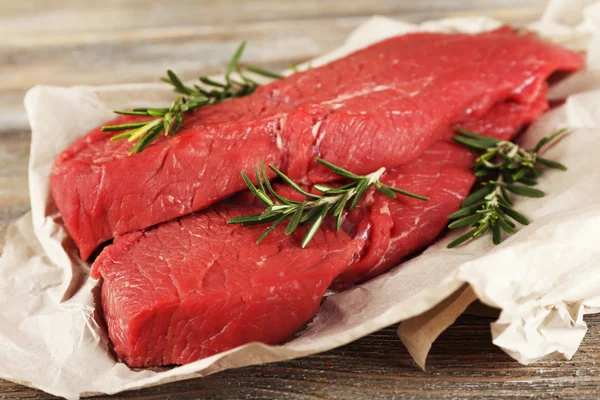Rauwe biefstuk met rozemarijn op papier op houten achtergrond — Stockfoto