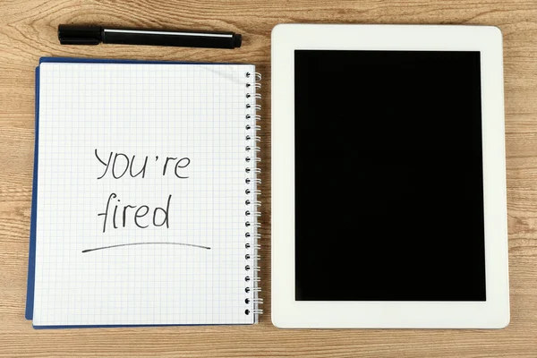 Message You 're Fired on notebook with marker and tablet on wooden table, top view — стоковое фото