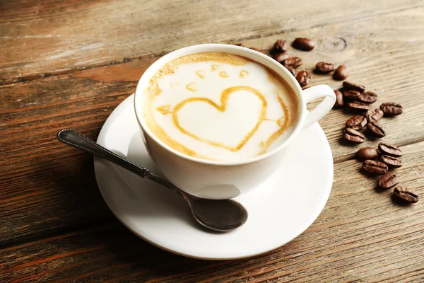 Tasse de café latte art avec des grains sur fond en bois — Photo