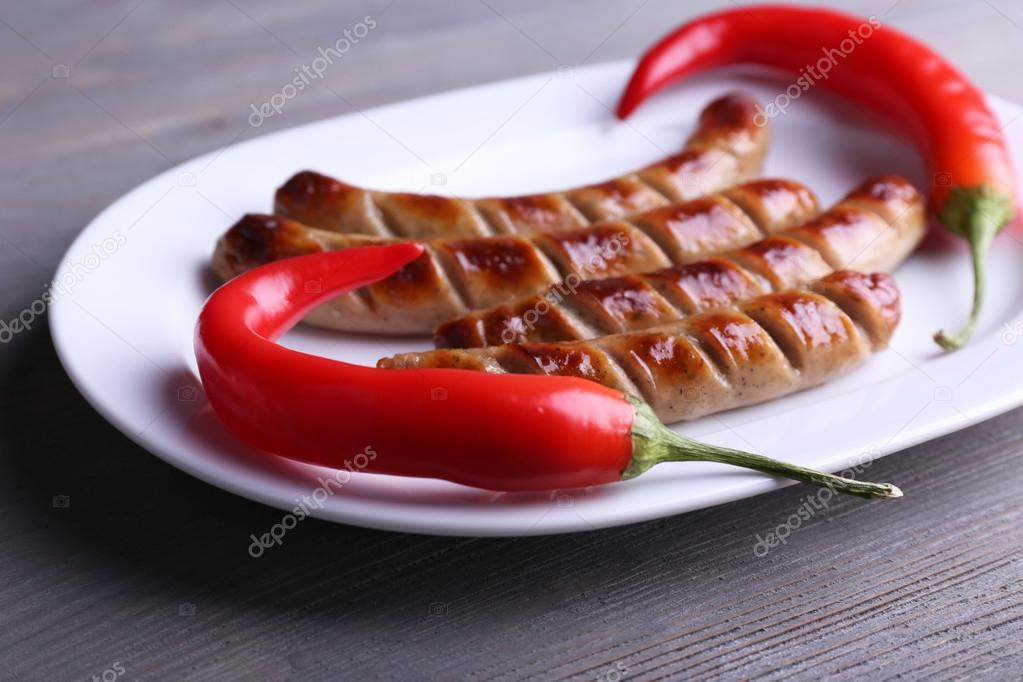 Grilled sausages on plate with chili pepper on table close up