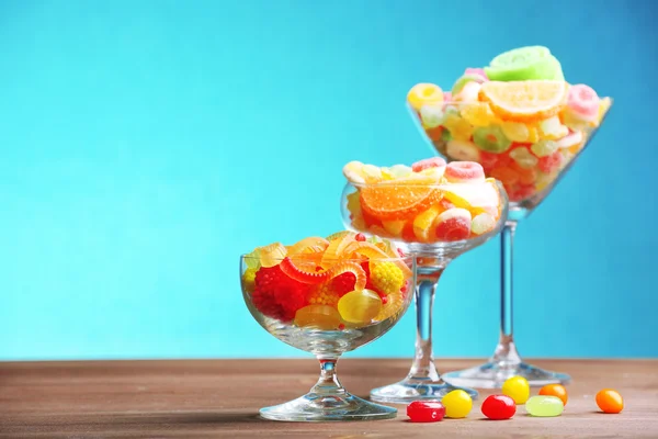 Kleurrijke snoepjes in glazen op tafel op blauwe achtergrond — Stockfoto