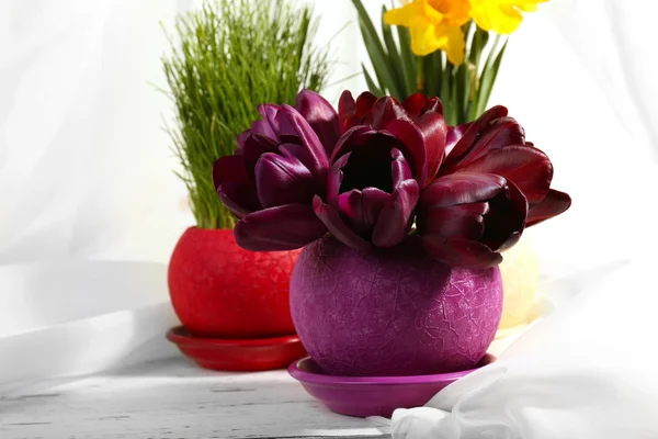 Bellissimi fiori con erba verde in vasi su sfondo tessuto — Foto Stock