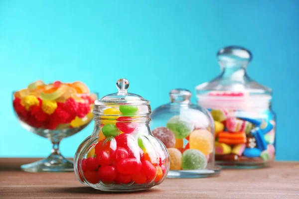 Kleurrijke snoepjes in potten op tafel op blauwe achtergrond — Stockfoto