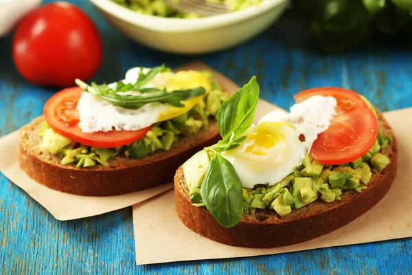 Sabroso sándwich con huevo, aguacate y verduras en servilleta de papel, sobre fondo de madera de color — Foto de Stock