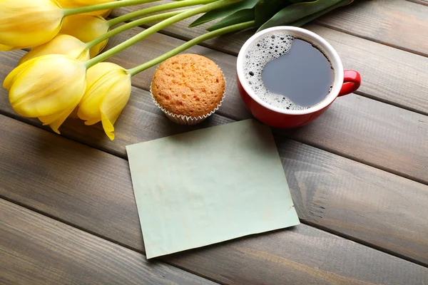 Tasse de café avec cupcake frais, tulipes et feuille de papier vierge sur fond en bois — Photo