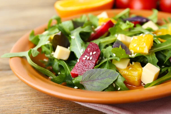 Leckerer Salat mit Rucolablättern im Teller auf Holztisch, Nahaufnahme — Stockfoto
