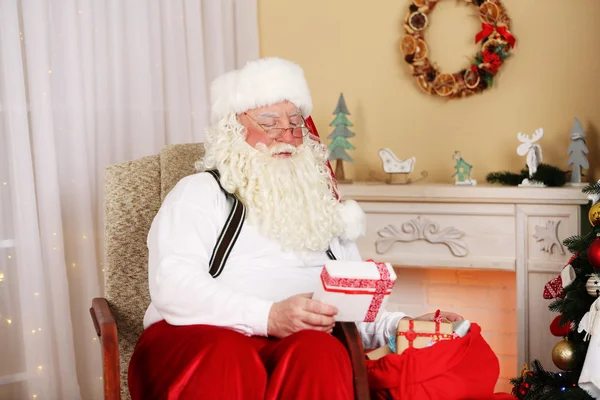 Santa Claus zitten met kinderen presenteert in comfortabele stoel in de buurt van open haard thuis — Stockfoto