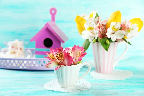 Beautiful flowers in cup, on color wooden background — Stock Photo, Image