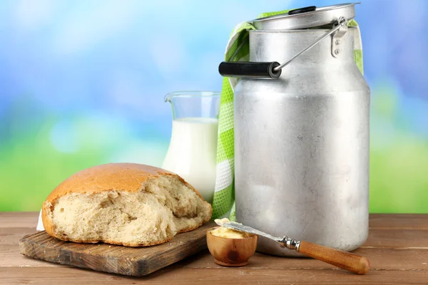 Retro can for milk with fresh bread and jug of milk on wooden table, on bright background. Bio products concept — Stock Photo, Image