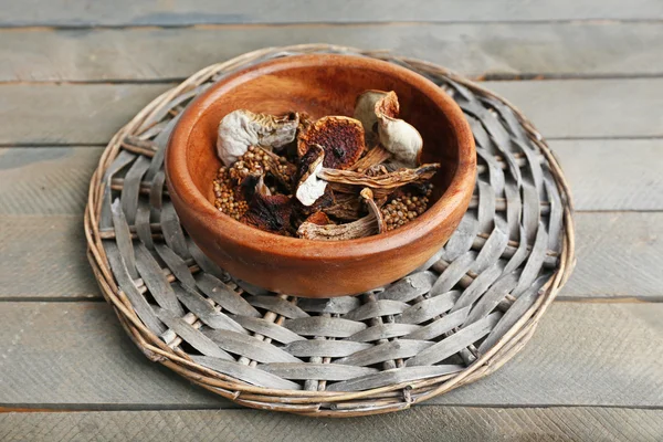 Dried mushrooms in bowl on wicker mat on wooden background — Stock Photo, Image