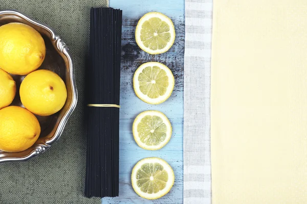 Černé špagety a citrony na dřevěný stůl horní pohled — Stock fotografie