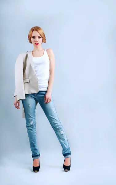 Mooie jonge vrouw in jas en jeans poseren op lichte achtergrond — Stockfoto