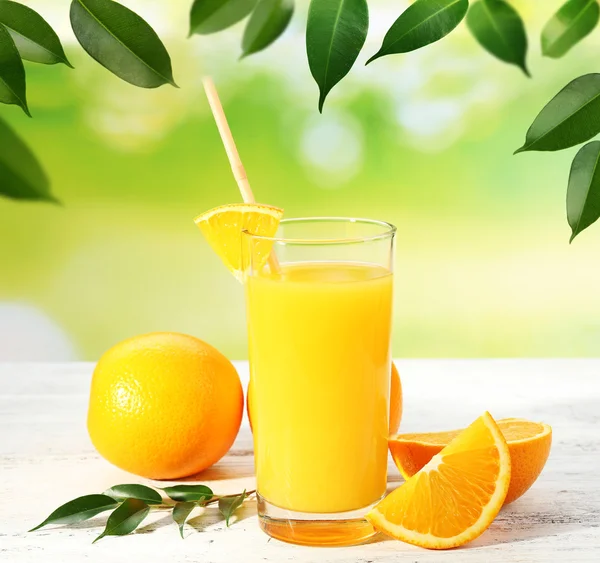 Glas sinaasappelsap en sinaasappelen op houten tafel en natuurlijke achtergrond — Stockfoto