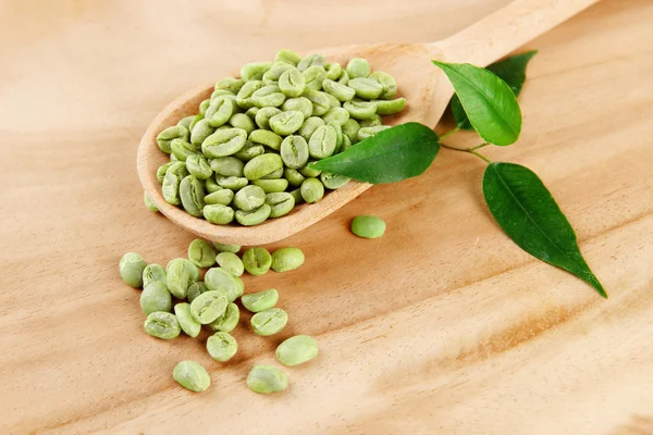 スプーンや木製の背景に葉の緑のコーヒー豆 — ストック写真
