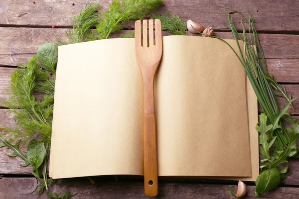 Buka buku resep dengan herbal segar dan rempah-rempah di latar belakang kayu — Stok Foto