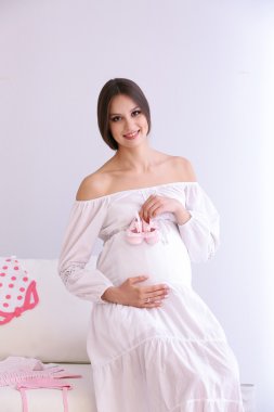 Hamile kadınla odasında kanepede oturan bebek patik