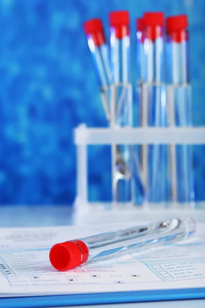 Test tubes and clipboard with medical history form on table on blue background — Stockfoto