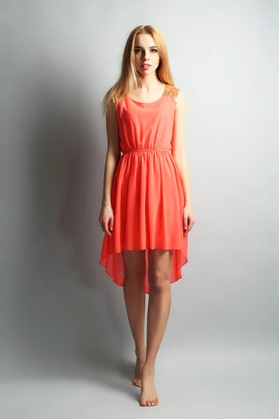 Ausdrucksstarkes junges Model in orangefarbenem Kleid auf grauem Hintergrund — Stockfoto