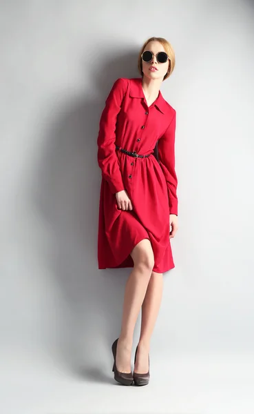 Kırmızı elbise ve gri arka plan üzerinde güneş gözlüğü ifade genç model — Stok fotoğraf