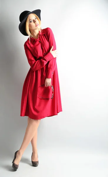 Ekspresyjny młody model w czerwoną sukienkę i czarny kapelusz na szarym tle — Zdjęcie stockowe
