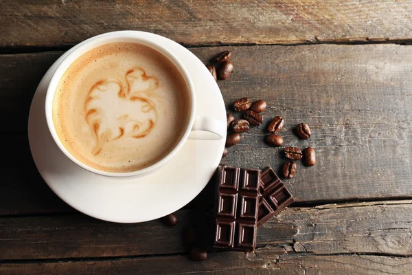 Cup of coffee latte art with grains and chocolate on wooden background — Stock Photo, Image