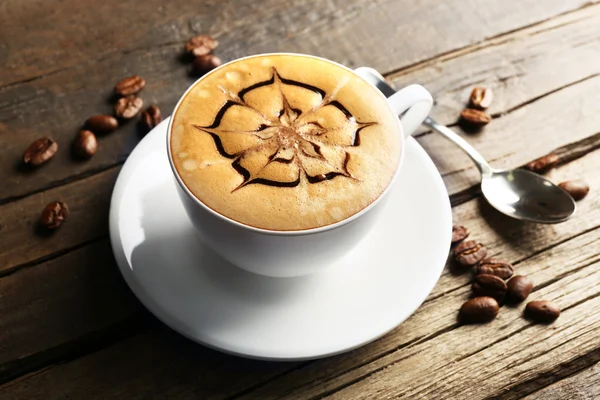 Xícara de café arte latte com grãos em fundo de madeira — Fotografia de Stock