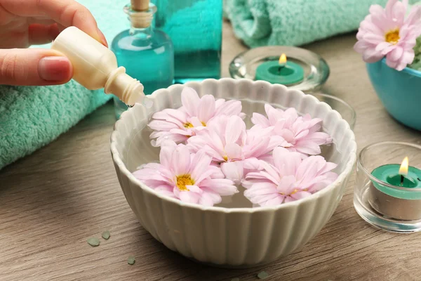 Female hand with bottle of essence and bowl of aroma spa water on wooden table, closeup — Stock Photo, Image