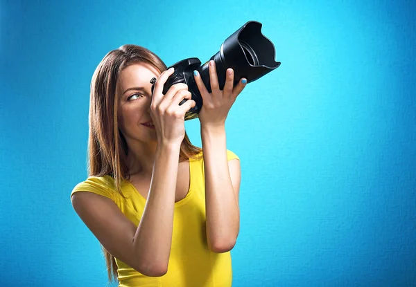 Ung kvinnlig fotograf tar bilder på blå bakgrund — Stockfoto