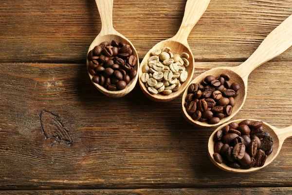 Kaffeebohnen in Löffeln auf Holzgrund — Stockfoto