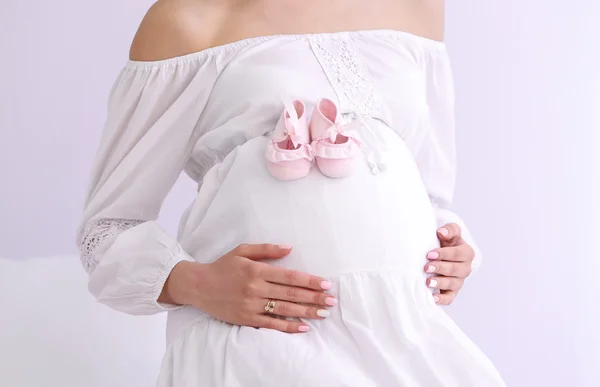 白い壁の背景に赤ちゃんの bootees と妊娠中の女性 — ストック写真