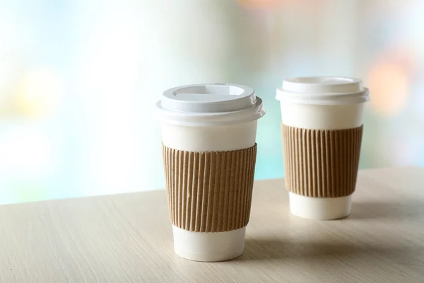 Бумажные чашки кофе на столе на ярком фоне — стоковое фото