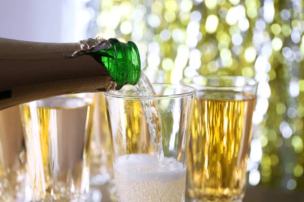 Pouring champagne from bottle into glasses on bright background — Stock Photo, Image