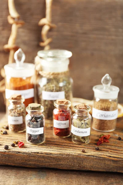 Surtido de especias en botellas de vidrio sobre tabla de cortar, sobre fondo de madera — Foto de Stock