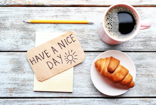 Cup of coffee with fresh croissant and Have A Nice Day massage on wooden table, top view — Stock Photo, Image