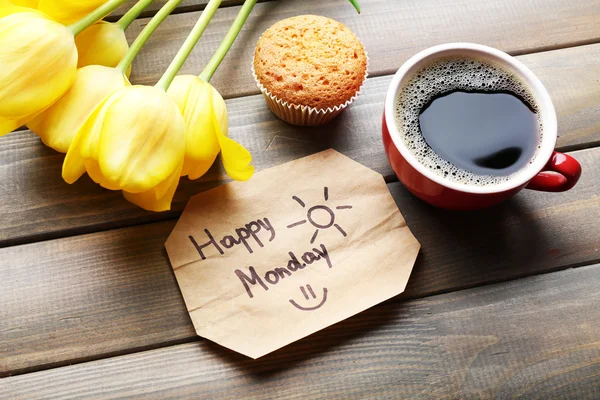 Cup of coffee with fresh cupcake, tulips and Happy Monday massage on wooden background