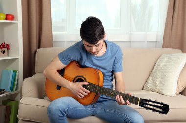 Odadaki kanepede gitarlı genç adam.