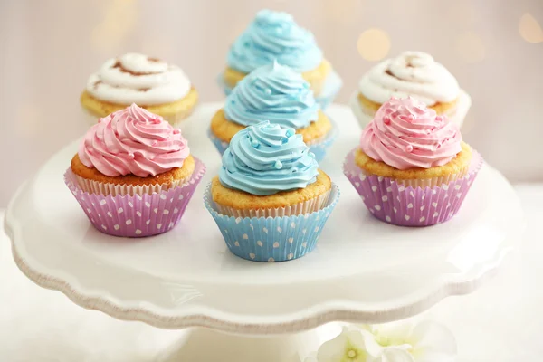 Deliciosos cupcakes en pie de pastel en la mesa sobre fondo claro — Foto de Stock