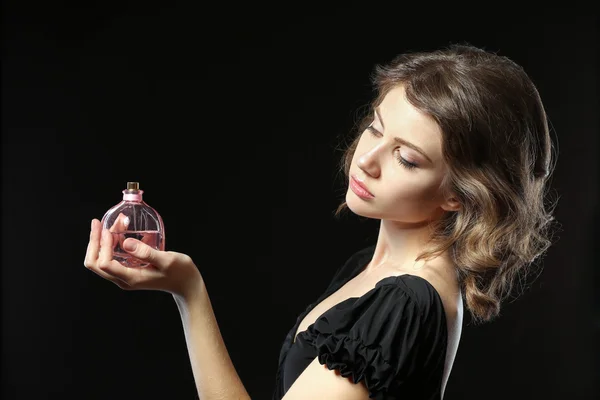 Красивая женщина с духами бутылку на черном фоне — стоковое фото