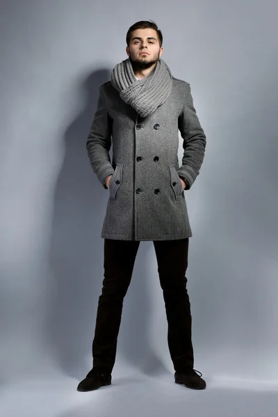 Young man in coat on gray background — Stock Photo, Image