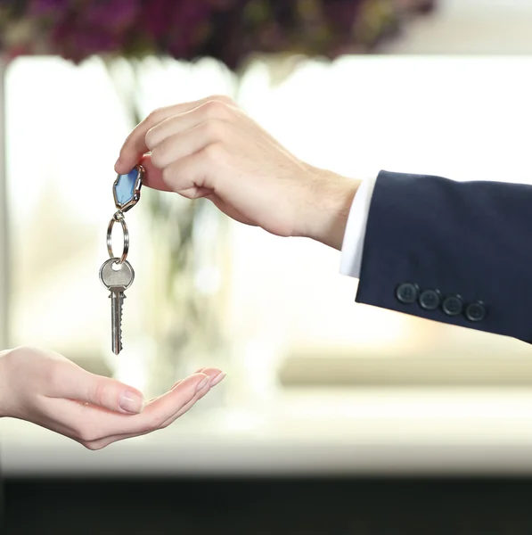 Hand of businessman giving keys to female hand on blurred background — Stock Photo, Image